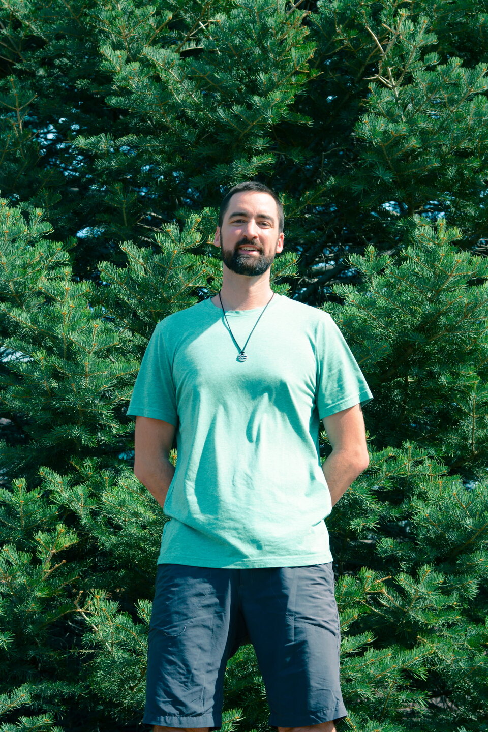 Brandon Pogge standing outdoors in front of pine trees.